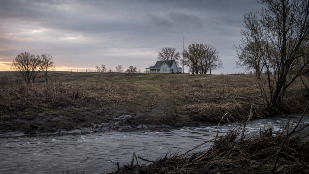 Illustrative rural Kansas farmhouse and creek under an overcast sky