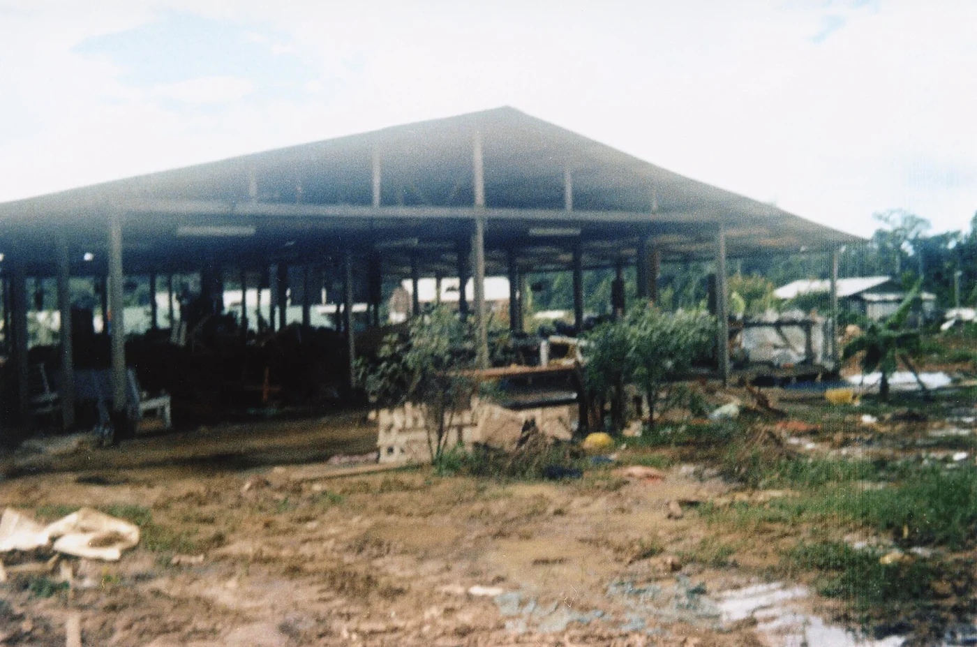 The empty open-sided pavilion at Jonestown, photographed after the deaths, with debris on the muddy ground in front.